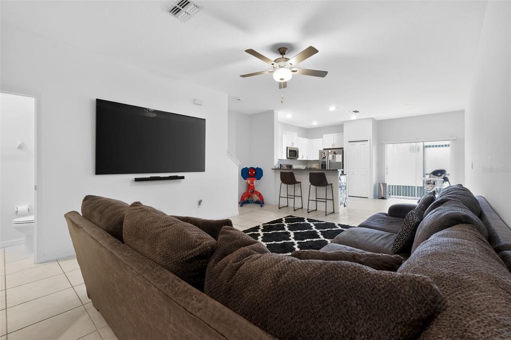 A living room with a large sectional sofa, wall-mounted television, and an open-concept kitchen — 32021 POWDERPUFF MIMOSA DRIVE, SAN ANTONIO, FL