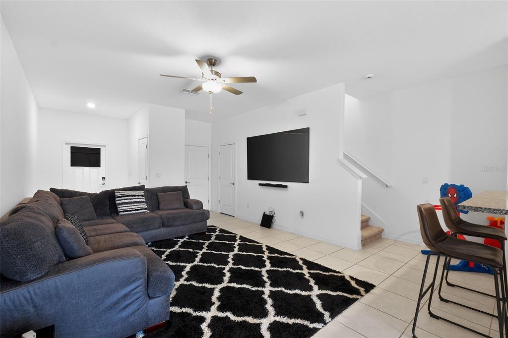 A living room features a dark sectional sofa, a black patterned rug, and a wall-mounted television — 32021 POWDERPUFF MIMOSA DRIVE, SAN ANTONIO, FL