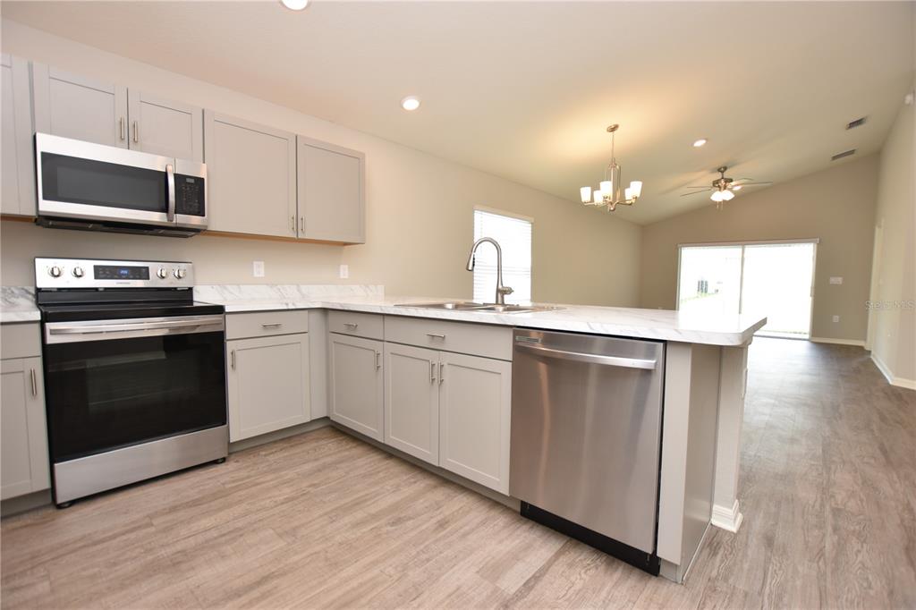 A kitchen features light gray cabinets, stainless steel appliances, and a white marble-look countertop — 372 CASCARA LANE, AUBURNDALE, FL