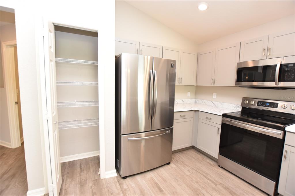 A kitchen features stainless steel appliances, light gray cabinets, white marble-look countertops, and a pantry — 372 CASCARA LANE, AUBURNDALE, FL