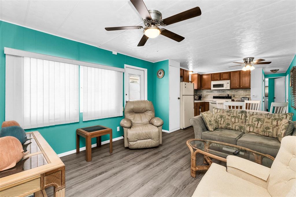 A living room with teal walls, wood-look flooring, a ceiling fan, and an open kitchen — 6442 HIKINA DRIVE, NORTH PORT, FL