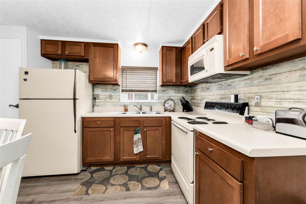 A kitchen features wood cabinets, white appliances, a light-colored countertop, and a wood-look backsplash — 6442 HIKINA DRIVE, NORTH PORT, FL