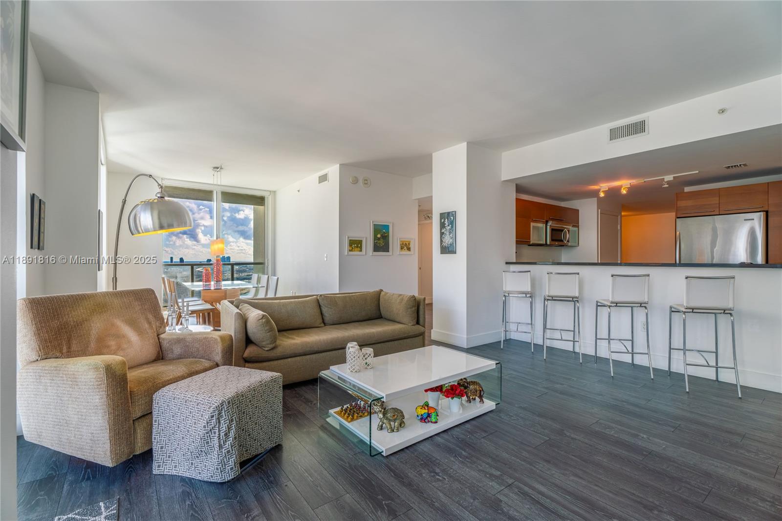A living room with a sofa, armchair, glass coffee table, and an open kitchen area — 253 NE 2nd St # 3203, Miami FL 33132, MIAMI, FL