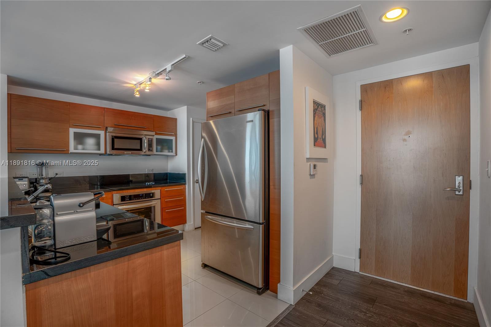 A kitchen features wood cabinets, stainless steel appliances, black countertops, and a wooden entry door — 253 NE 2nd St # 3203, Miami FL 33132, MIAMI, FL