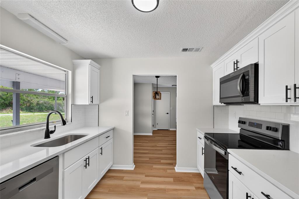 A kitchen features white cabinets, stainless steel appliances, a sink, and light wood flooring — 12071 DEEP CREEK DRIVE, SPRING HILL, FL