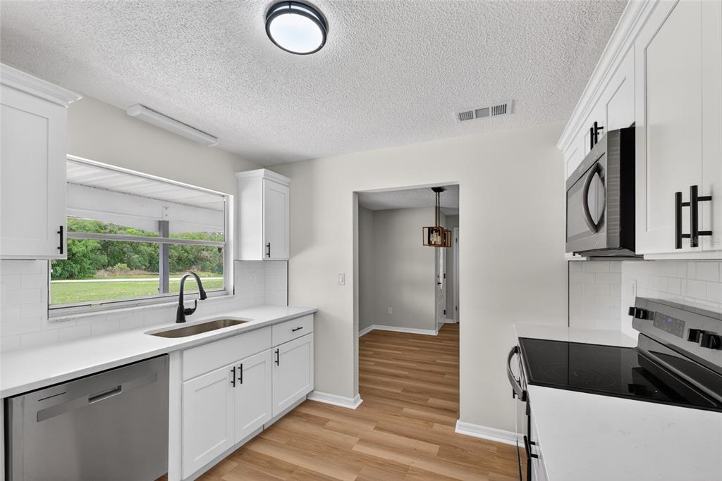 A kitchen with white cabinets, stainless steel appliances, a window, and wood-look flooring — 12071 DEEP CREEK DRIVE, SPRING HILL, FL