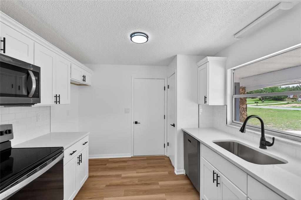 A kitchen with white cabinets, black hardware, stainless steel appliances, and wood-look flooring — 12071 DEEP CREEK DRIVE, SPRING HILL, FL