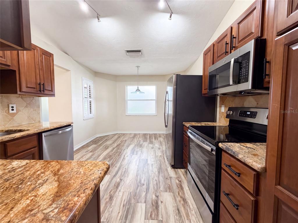 A kitchen features wood cabinets, granite countertops, stainless steel appliances, and wood-look flooring — 3430 55TH DRIVE E, BRADENTON, FL