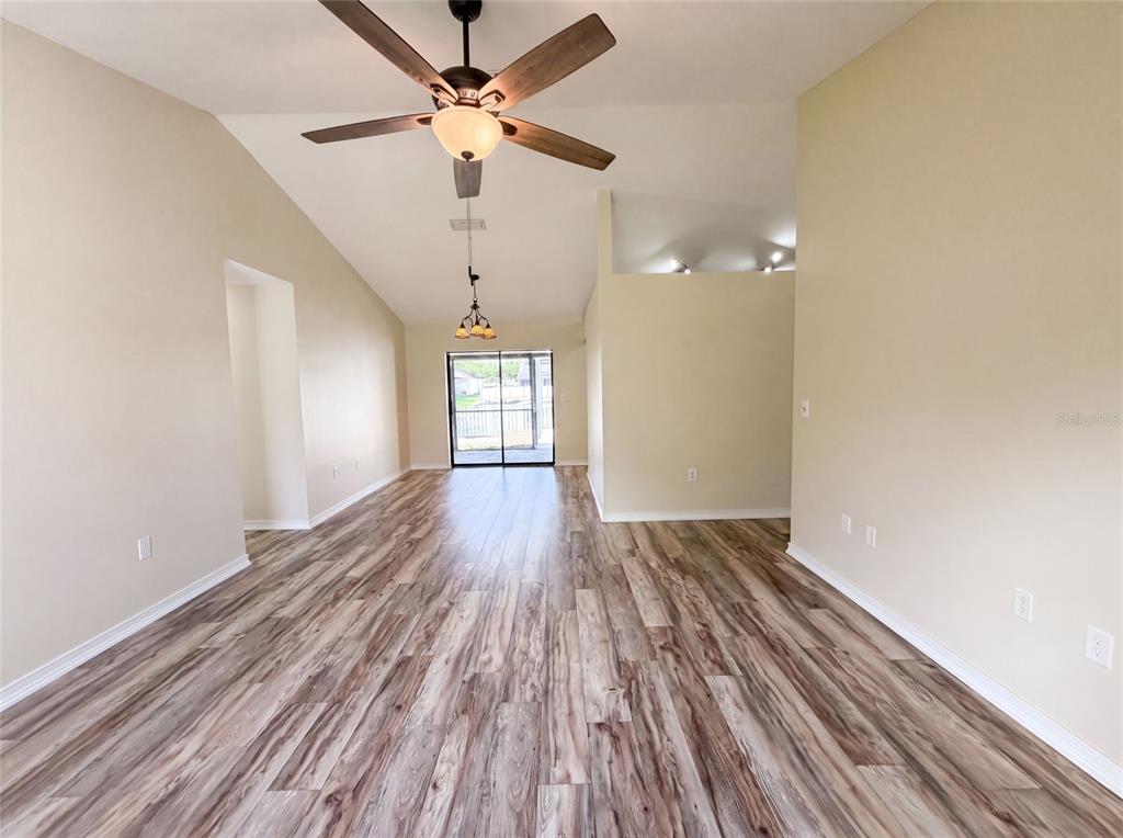 An open-concept living area features vaulted ceilings, wood-look flooring, and a sliding glass door — 3430 55TH DRIVE E, BRADENTON, FL