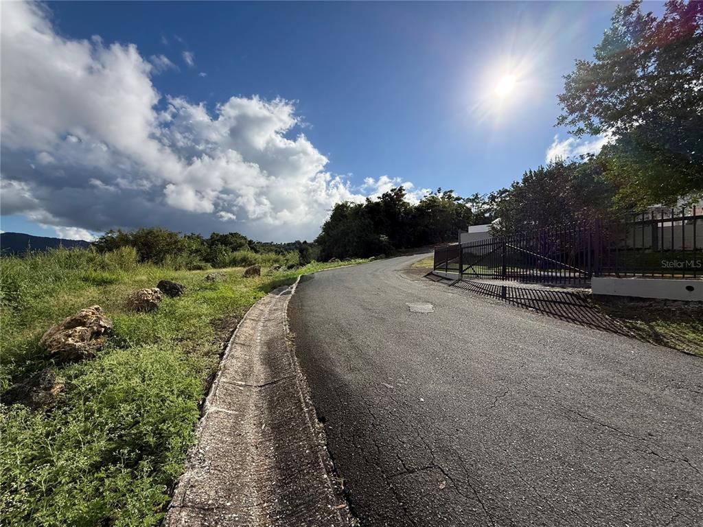 A paved road curves past a grassy hillside with rocks under a sunny sky — Carr 185 . UNIT F, CAROLINA, PR