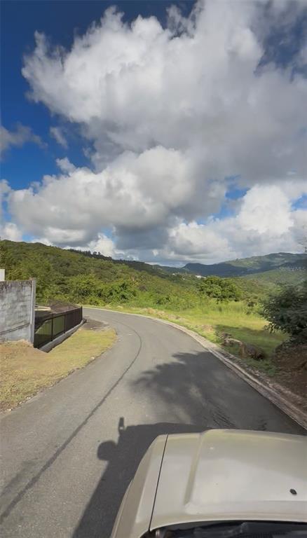 A view from a vehicle looking down a paved road toward rolling green hills — Carr 185 . UNIT F, CAROLINA, PR