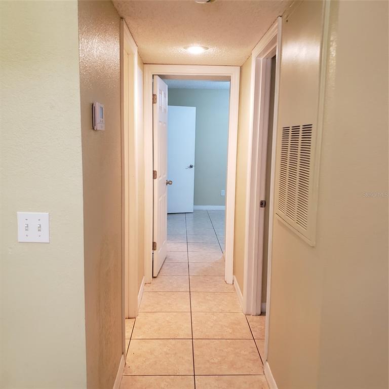 A hallway with beige tile flooring leads to an open doorway showing a bedroom — 5168 CONROY ROAD UNIT 11, ORLANDO, FL