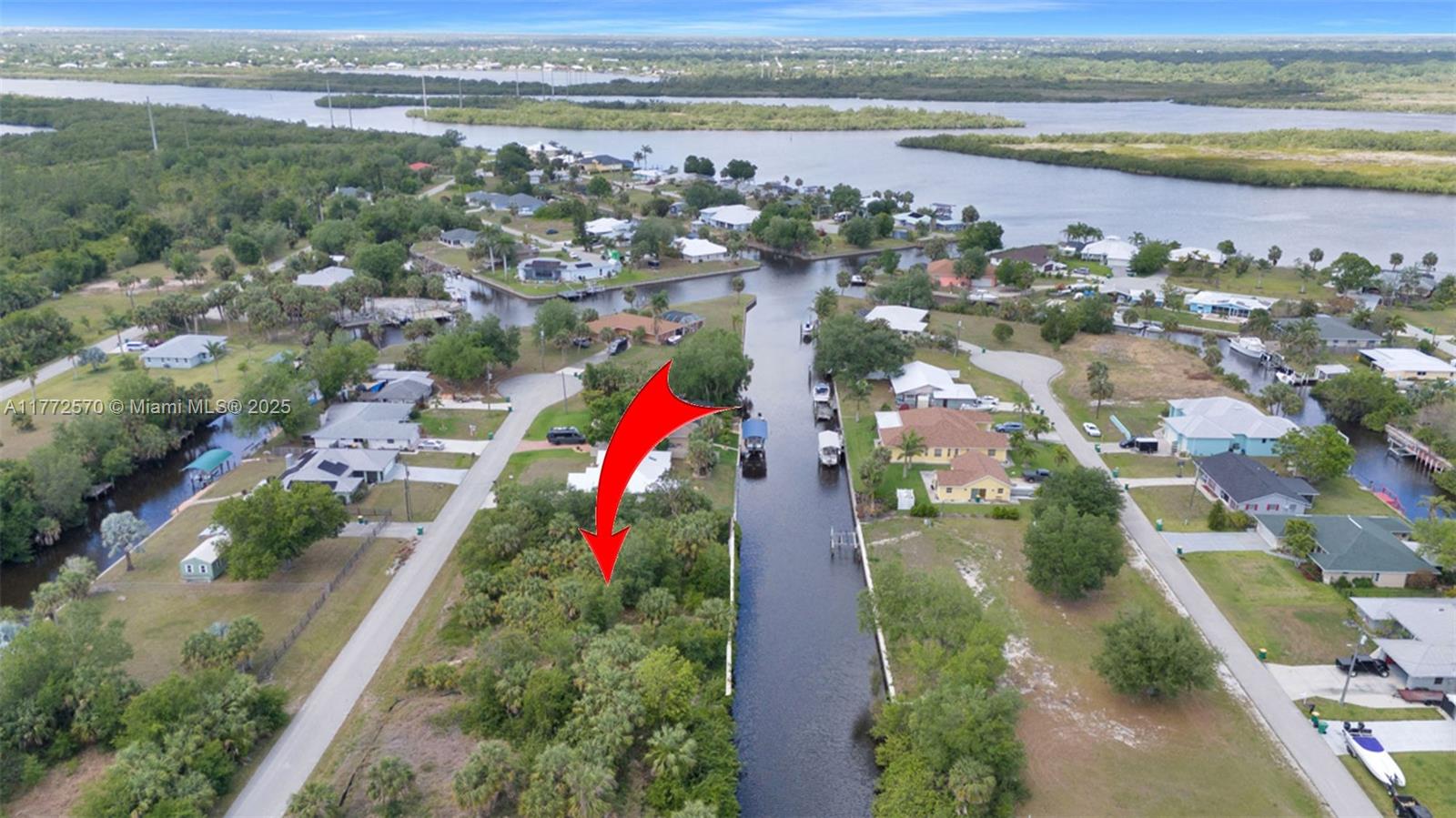 An aerial view shows a vacant, tree-covered waterfront lot marked by a red arrow — 28450 Sabal Palm Dr, Punta Gorda FL 33982, PUNTA GORDA, FL