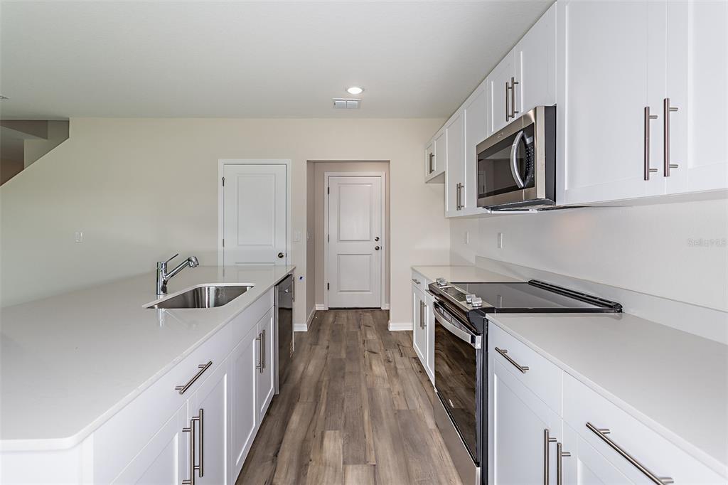 A modern kitchen features white cabinets, stainless steel appliances, quartz countertops, and wood-look flooring — 1756 VANILLA STREET, HAINES CITY, FL