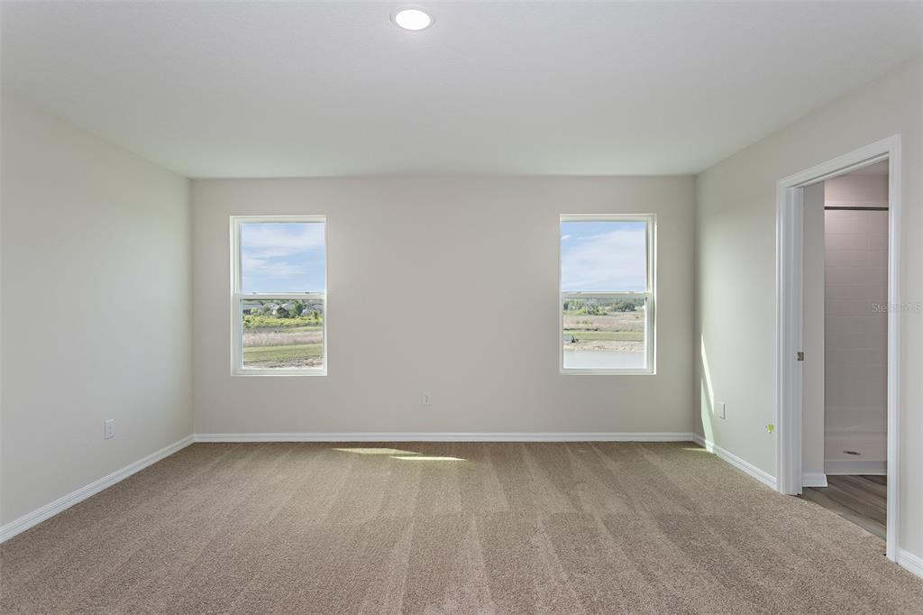 An empty bedroom with beige carpet, light walls, two windows, and an attached bathroom — 1756 VANILLA STREET, HAINES CITY, FL