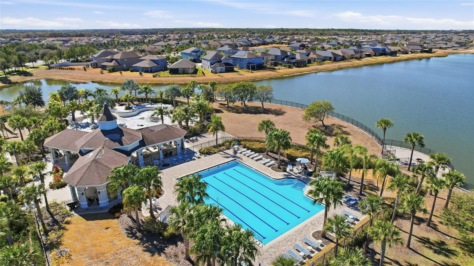 An aerial view of a community swimming pool and clubhouse next to a large lake — 9728 Channing Hill Drive, FL 33573, FL