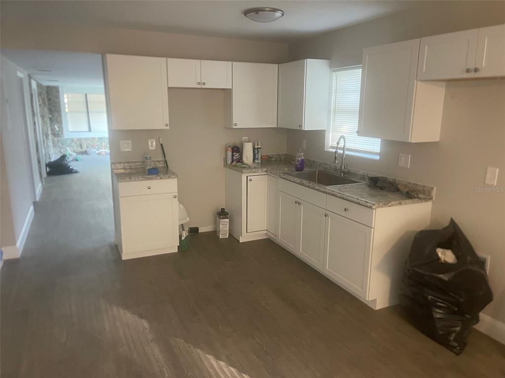 A kitchen features white cabinets, granite-look countertops, and light wood-style flooring — 401 MARTIN LUTHER KING JR AVENUE, WILDWOOD, FL