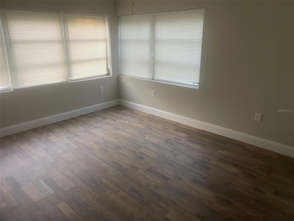 An empty room features wood-look flooring, light-colored walls, and windows covered with horizontal blinds — 401 MARTIN LUTHER KING JR AVENUE, WILDWOOD, FL