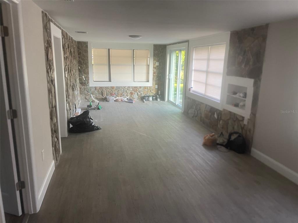 A room with light wood-look flooring, stone accent walls, and large windows — 401 MARTIN LUTHER KING JR AVENUE, WILDWOOD, FL