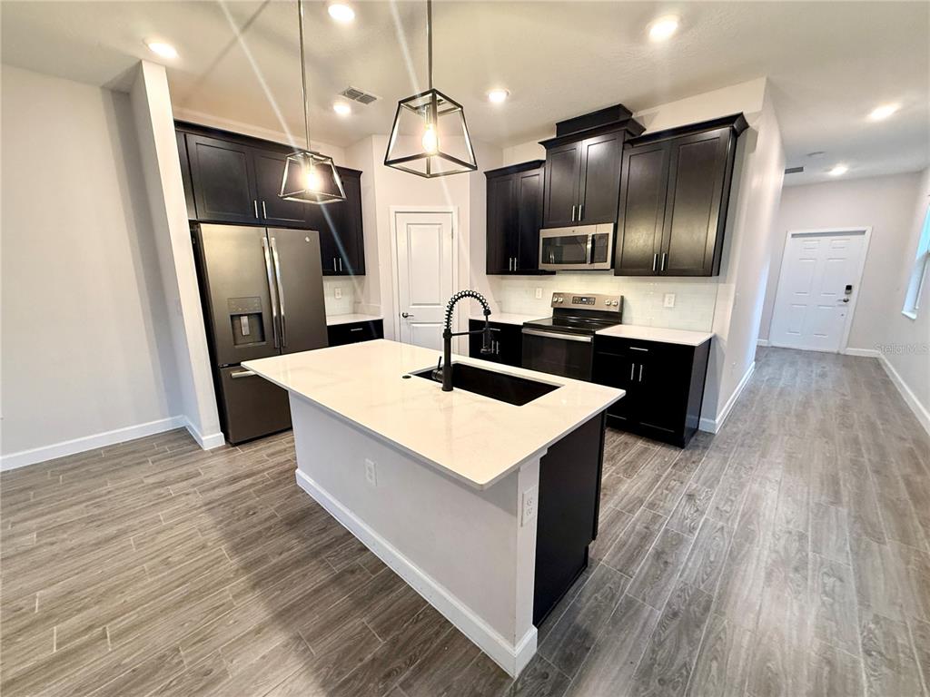 A modern kitchen features dark cabinets, stainless steel appliances, and a central white-topped island — 1421 HAPPY BIRD LANE, WINTER SPRINGS, FL