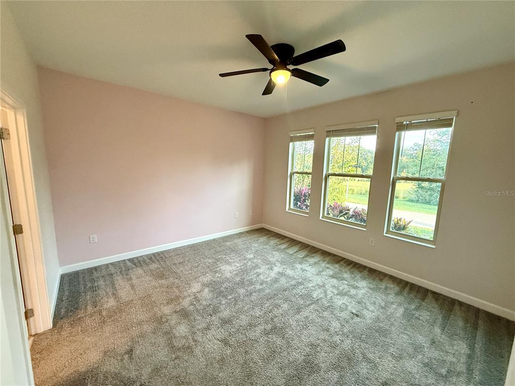An empty bedroom features light pink walls, gray carpeting, a ceiling fan, and three windows — 1421 HAPPY BIRD LANE, WINTER SPRINGS, FL