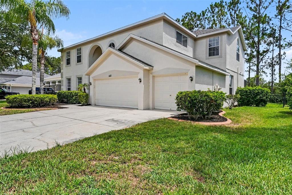 A two-story house with a three-car garage, beige stucco exterior, and a concrete driveway — 6112 CEZANNE AVENUE, LUTZ, FL