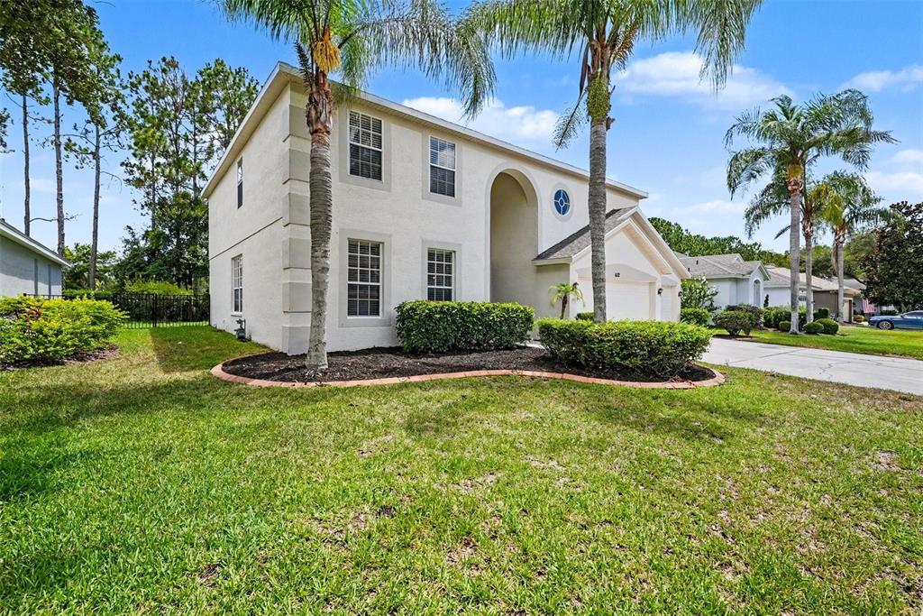 A two-story stucco house features a front-facing garage, palm trees, and a landscaped yard — 6112 CEZANNE AVENUE, LUTZ, FL