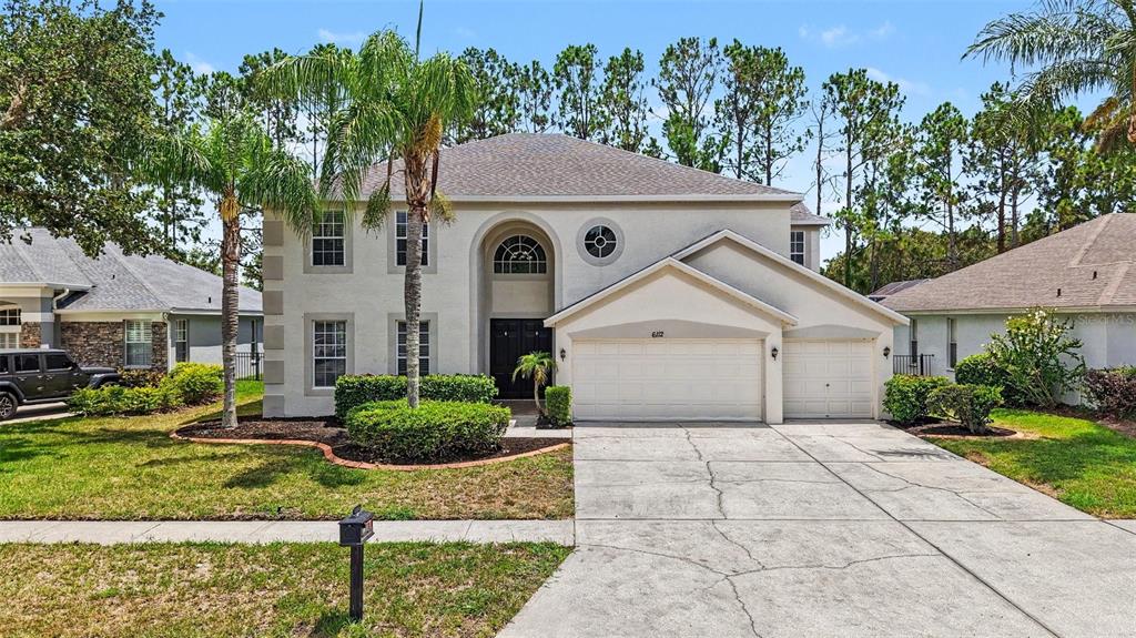 A two-story suburban house with a beige stucco exterior, a three-car garage, and palm trees — 6112 CEZANNE AVENUE, LUTZ, FL