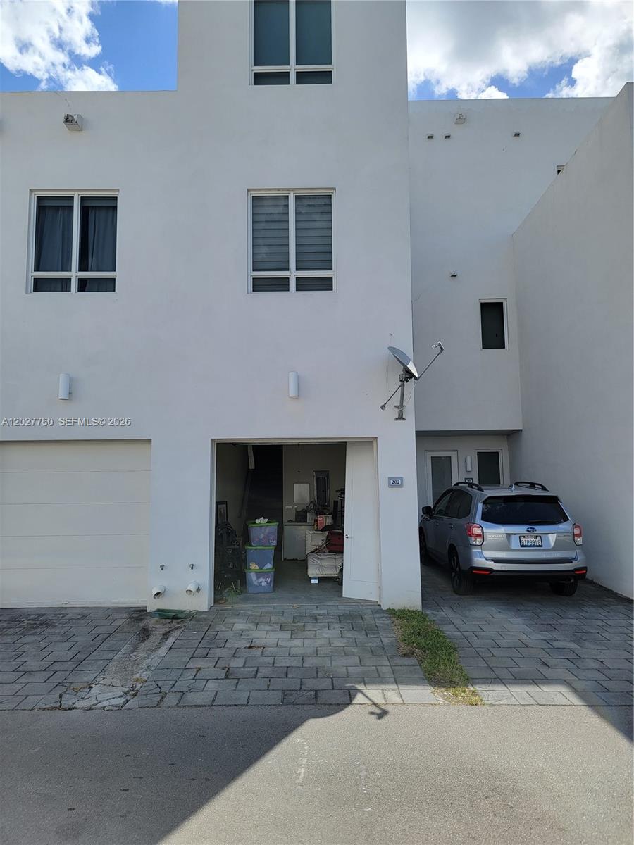 The exterior of a white multi-story townhouse features a garage, a driveway, and a parked car — 6310 NW 103rd Pl # 202, Doral FL 33178, DORAL, FL