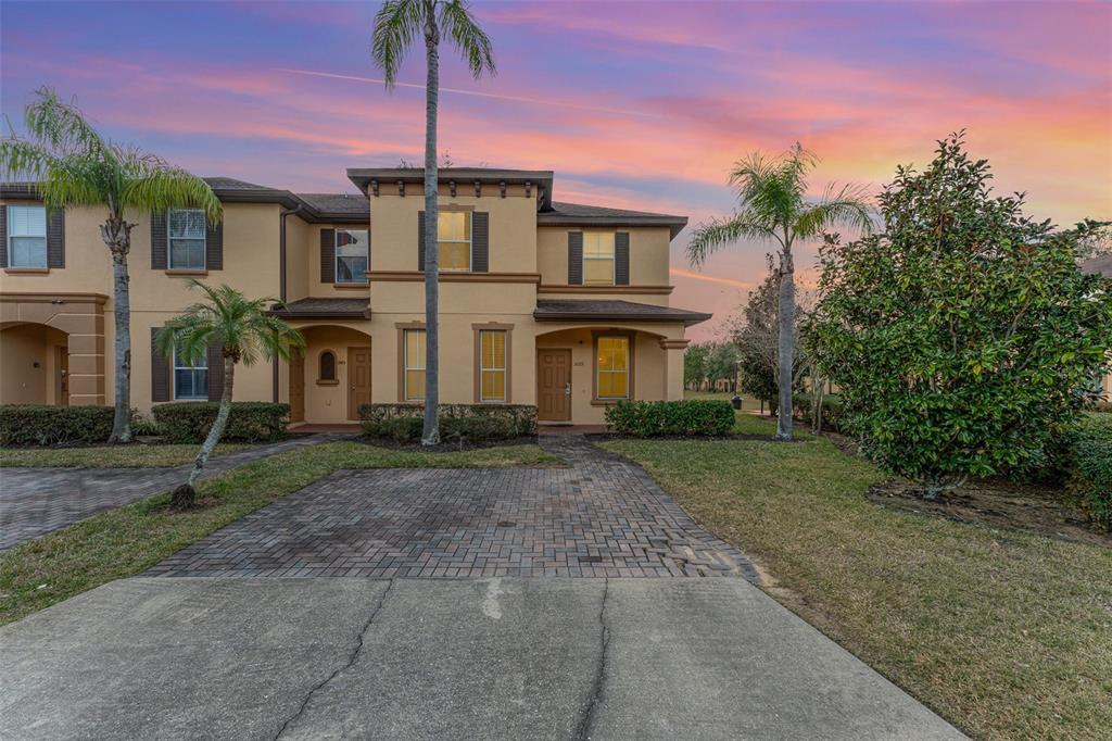 A two-story townhouse with a paved driveway, palm trees, and a sunset sky — 2153 CALABRIA AVENUE, DAVENPORT, FL
