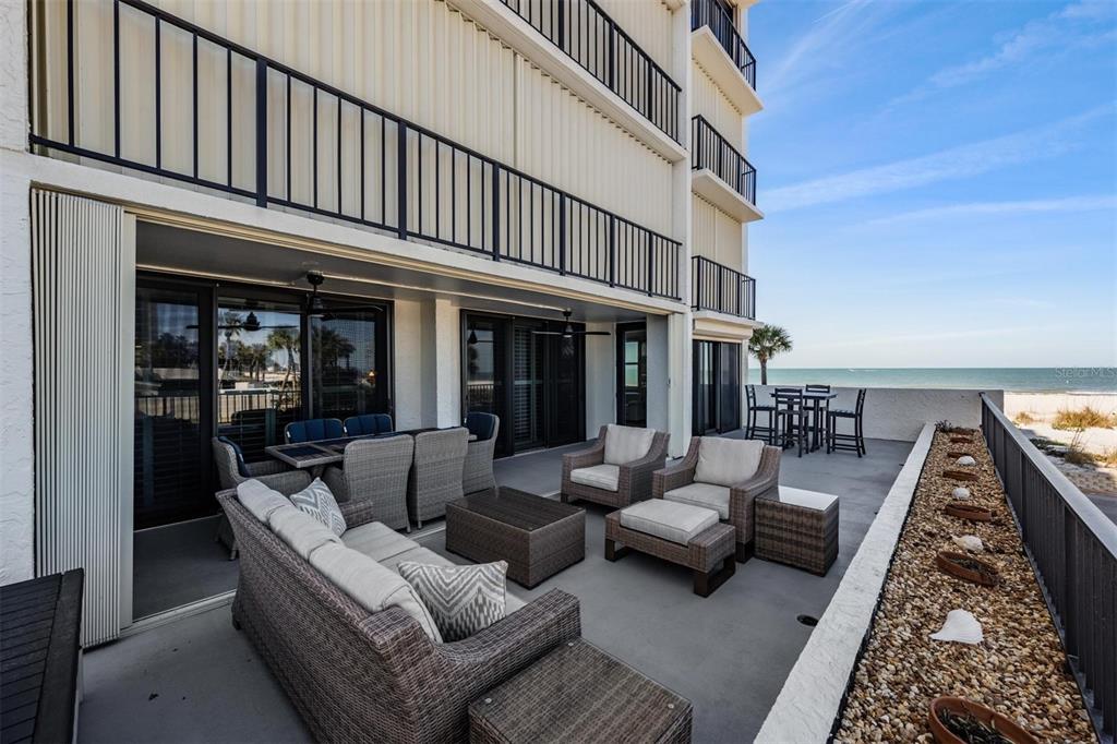 A spacious outdoor patio features wicker furniture, a dining set, and views of the ocean — 1400 GULF BOULEVARD UNIT 109, CLEARWATER BEACH, FL