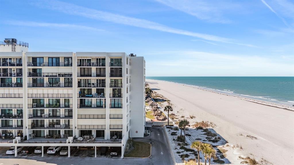 An aerial view shows a multi-story beachfront condominium building next to a sandy beach — 1400 GULF BOULEVARD UNIT 109, CLEARWATER BEACH, FL