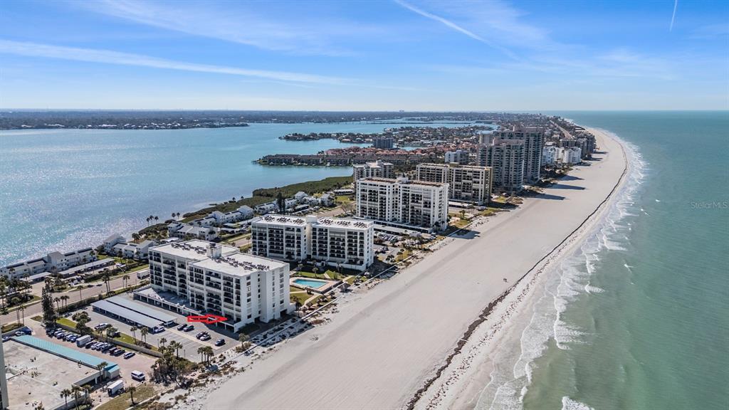 An aerial view shows a beachfront condominium complex with a parking area and pool — 1400 GULF BOULEVARD UNIT 109, CLEARWATER BEACH, FL
