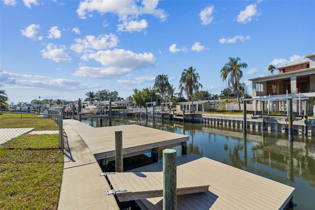 A wooden boat dock extends into a canal alongside a grassy yard and waterfront homes — 1733 BAYOU GRANDE BOULEVARD NE, ST PETERSBURG, FL