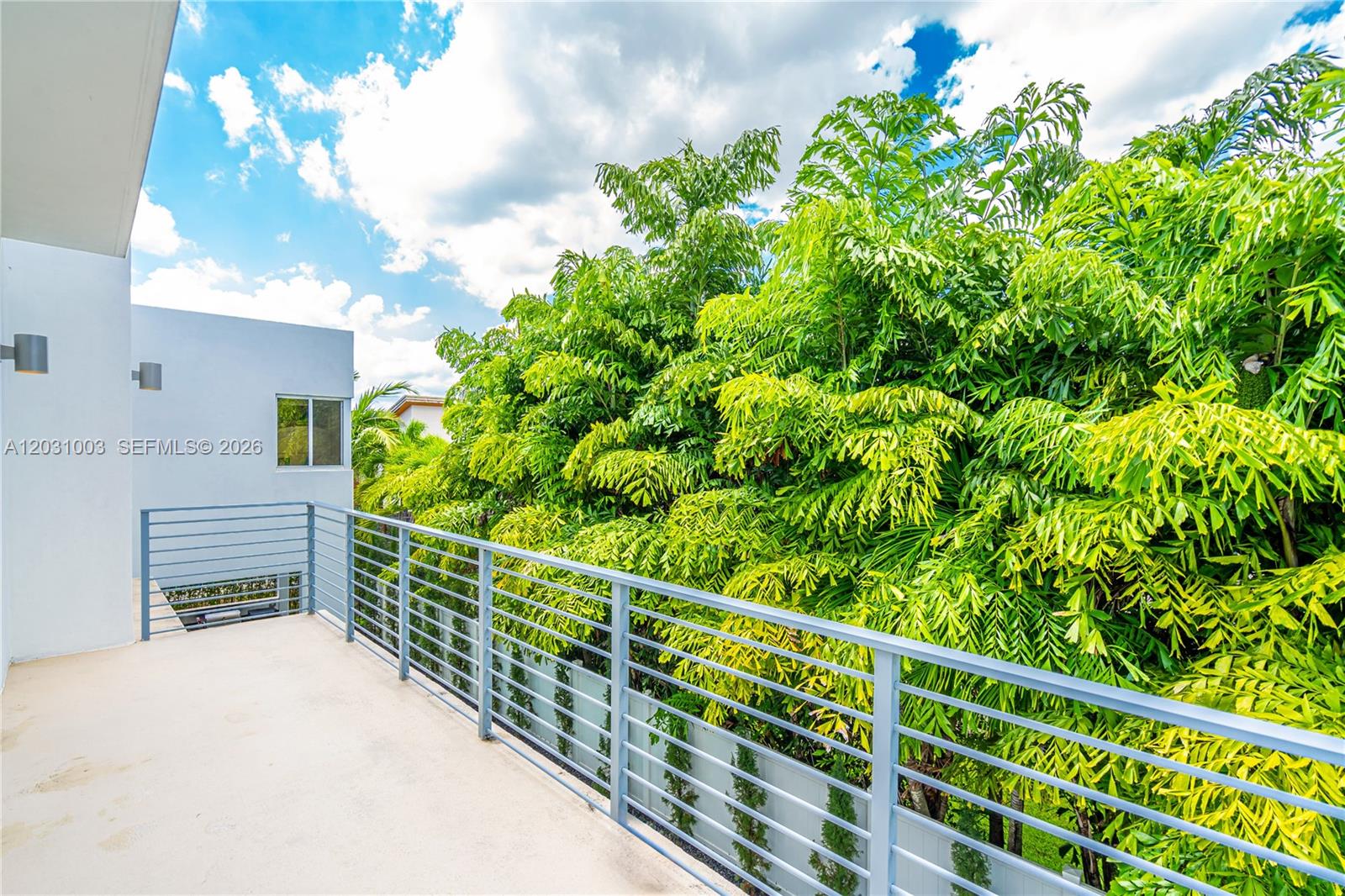 A modern balcony features a metal railing overlooking lush green trees under a blue sky — 10267 NW 75th Ter # 10267, Doral FL 33178, DORAL, FL