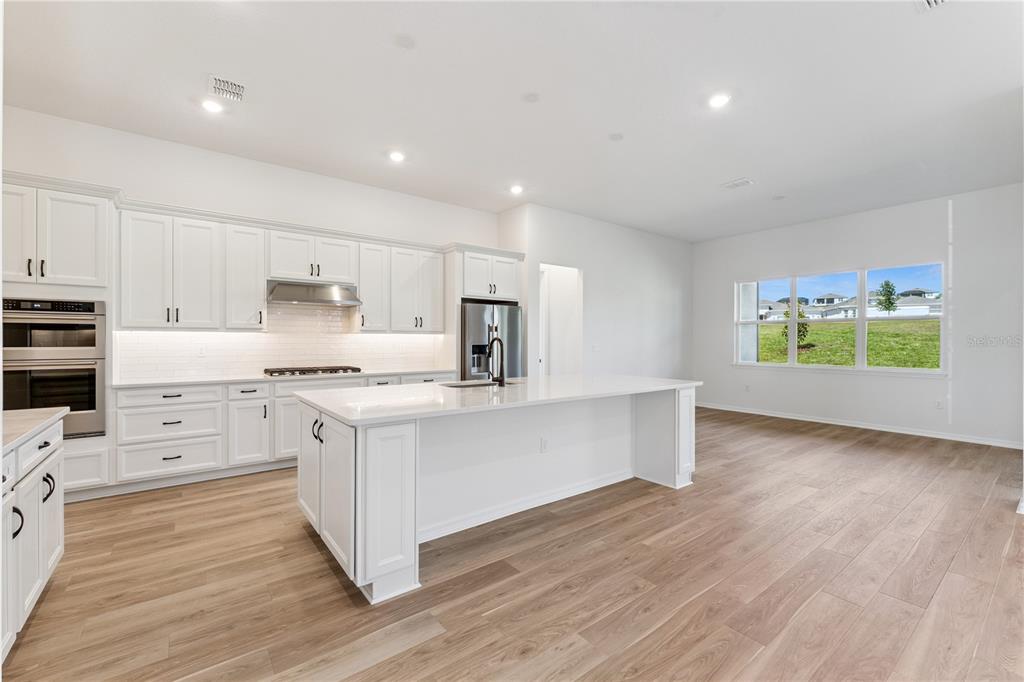 A modern kitchen features white cabinetry, a central island, and light wood-look flooring — 1552 SKYLINE HEIGHTS CIRCLE, MINNEOLA, FL