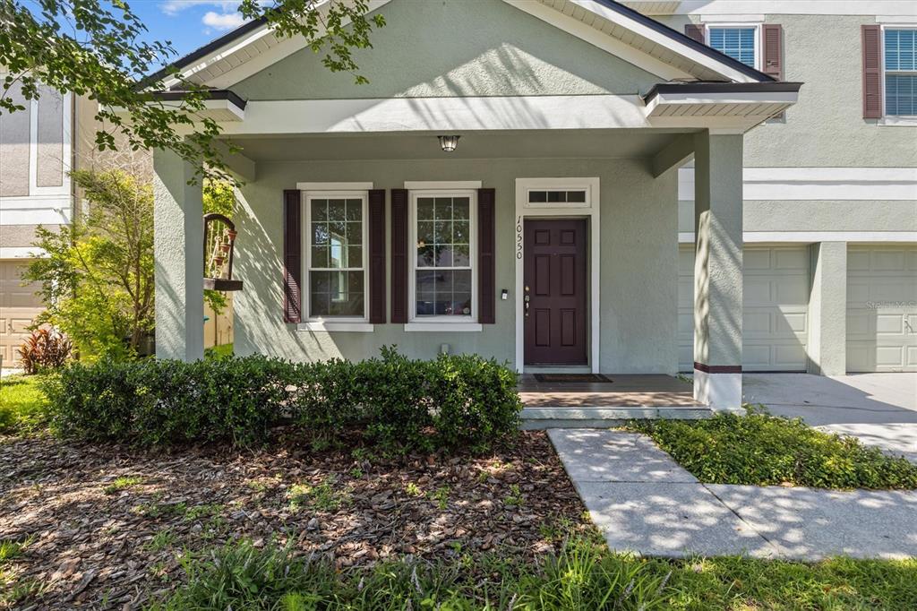 A light green house exterior features a covered front porch, dark shutters, and a garage — 10550 EASTPARK WOODS DRIVE, ORLANDO, FL