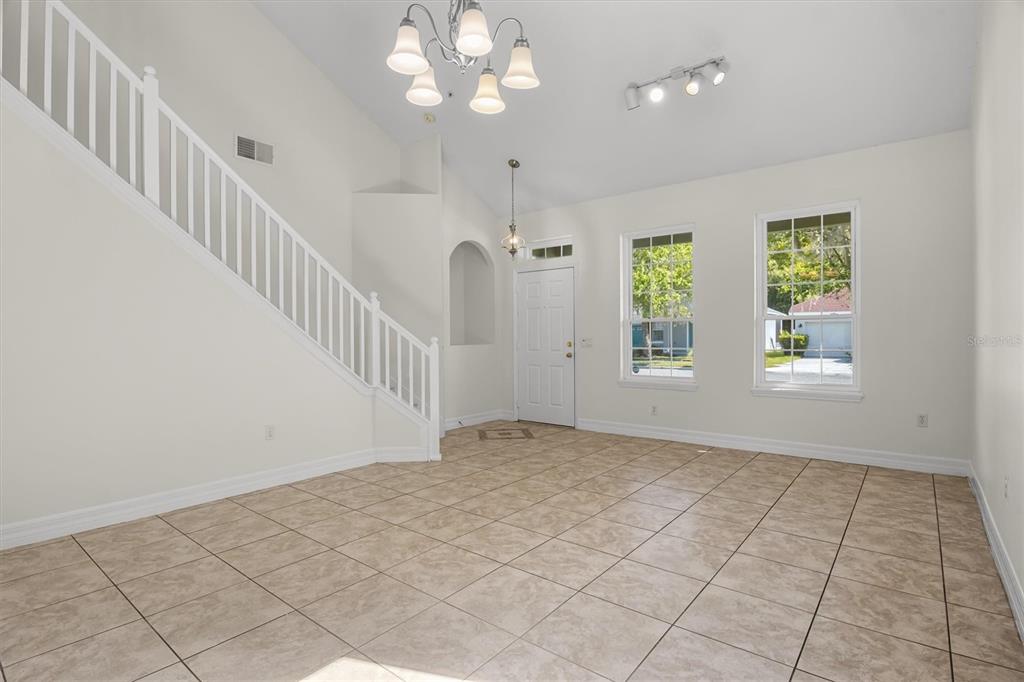 An empty room features tiled floors, a white staircase, a chandelier, and two large windows — 10550 EASTPARK WOODS DRIVE, ORLANDO, FL
