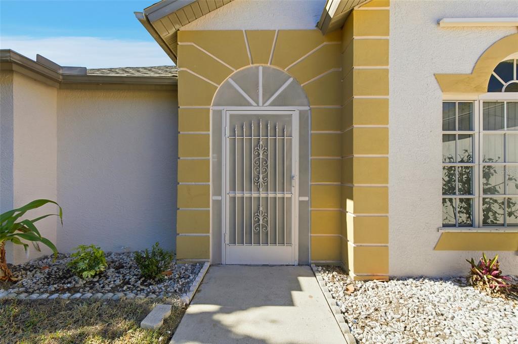 A white front door with a decorative security screen sits under an arched entryway — 191 ROSEMARY STREET, PORT CHARLOTTE, FL