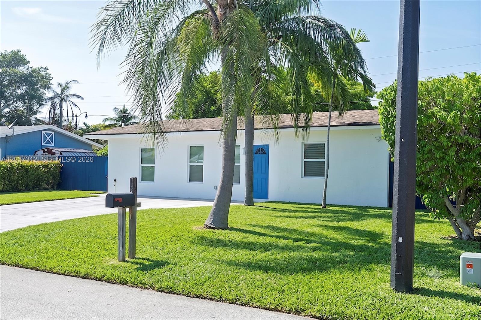 A white single-story house with a blue door and palm trees in the front yard — 1473 NE 30th Ct, Pompano Beach FL 33064, POMPANO BEACH, FL