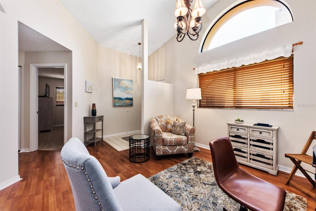 A living room features wood-look flooring, a patterned armchair, a chandelier, and a large window — 5656 ASHTON LAKE DRIVE UNIT 5656, SARASOTA, FL