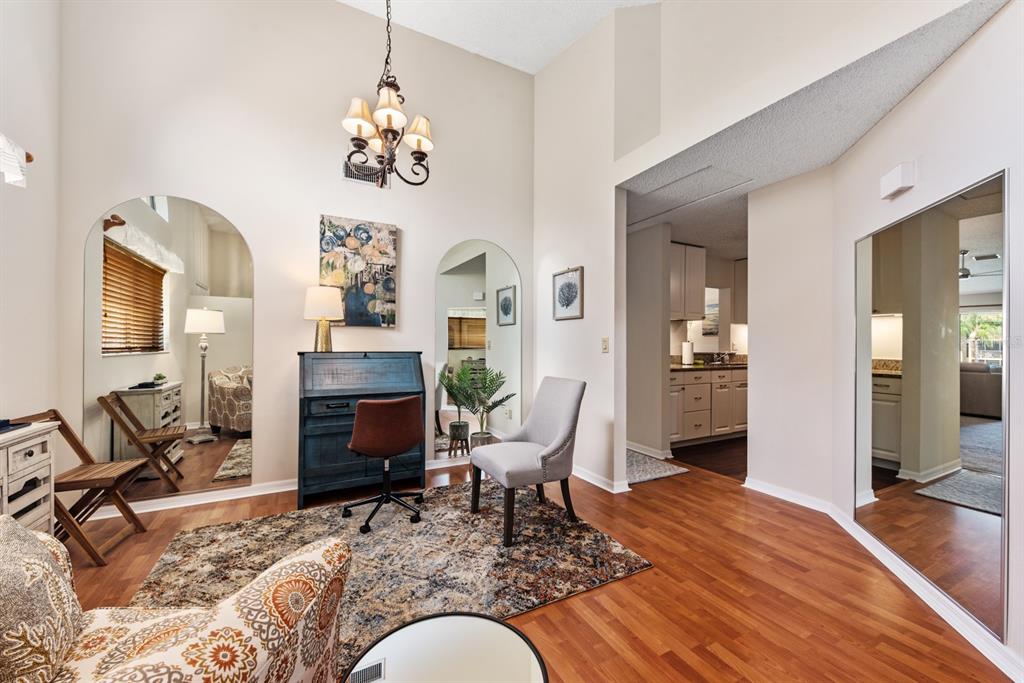 A room with wood floors, arched mirrors, a desk, and a chandelier leads to a kitchen — 5656 ASHTON LAKE DRIVE UNIT 5656, SARASOTA, FL