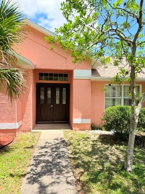 The exterior of a peach-colored house features a dark double-door entrance and a concrete walkway — 20 PALM LANE, PALM COAST, FL