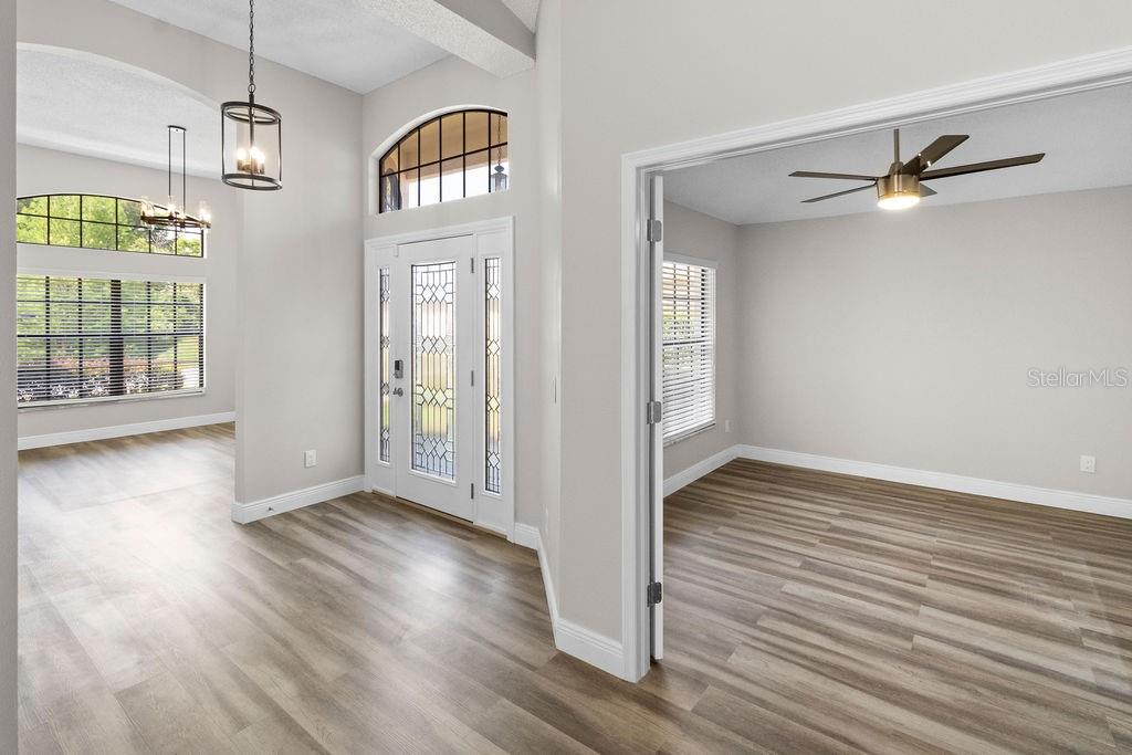A foyer with light wood-look flooring leads to a front door and an adjacent room — 9147 JIMINEZ DRIVE, HUDSON, FL