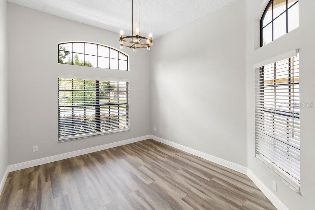 A bright room with light gray walls, wood-look flooring, a chandelier, and multiple windows — 9147 JIMINEZ DRIVE, HUDSON, FL