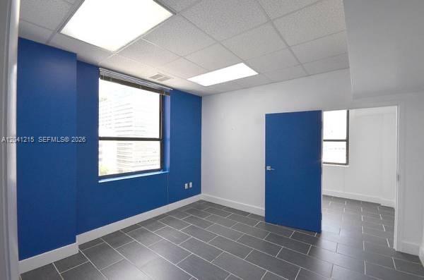 An empty office room features blue walls, gray tiled floors, and a large window — 168 SE 1st St # 501, Miami FL 33131, MIAMI, FL