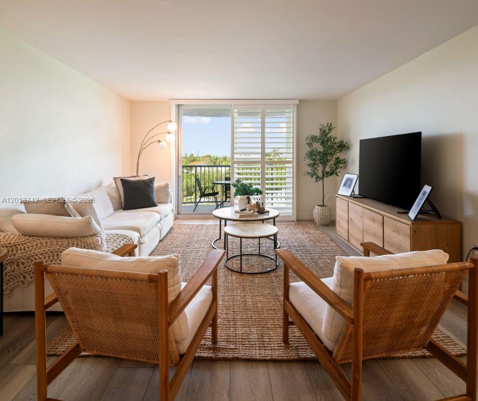 A living room features a white sofa, two wooden armchairs, a television, and a balcony — KEY BISCAYNE, FL