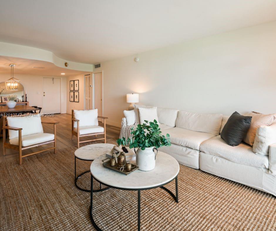 A living room features a white sofa, two round coffee tables, and two wooden armchairs — KEY BISCAYNE, FL
