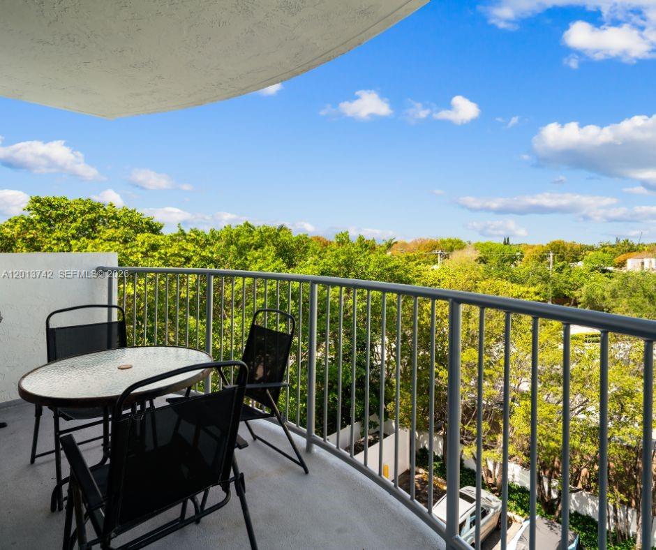A balcony with a small table and two chairs overlooks a tree-lined neighborhood — KEY BISCAYNE, FL