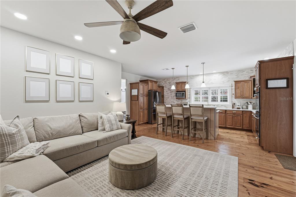 An open-concept living room and kitchen featuring a sectional sofa, island seating, and wood flooring — 1190 SUGAR BELT DRIVE, ST CLOUD, FL